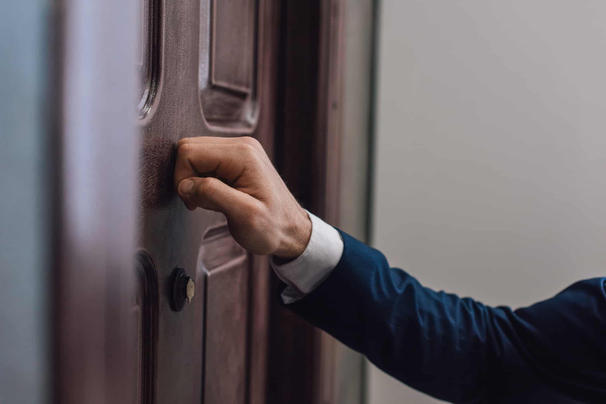 Man knocks on on a wooden front door.