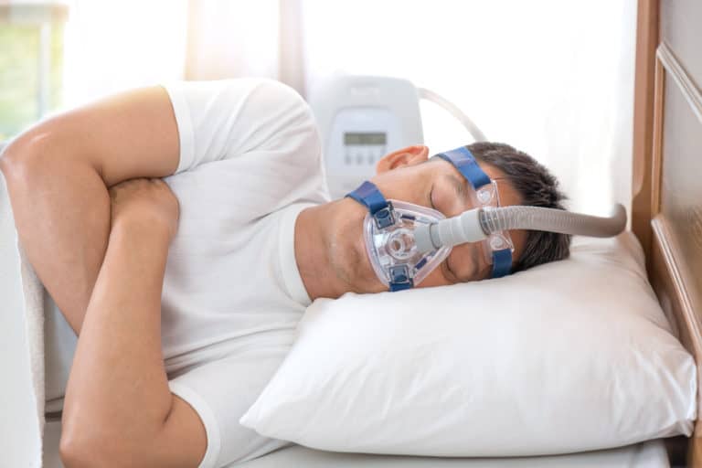 A man sleeping on his left side with a CPAP machine to help sleep apnoea.