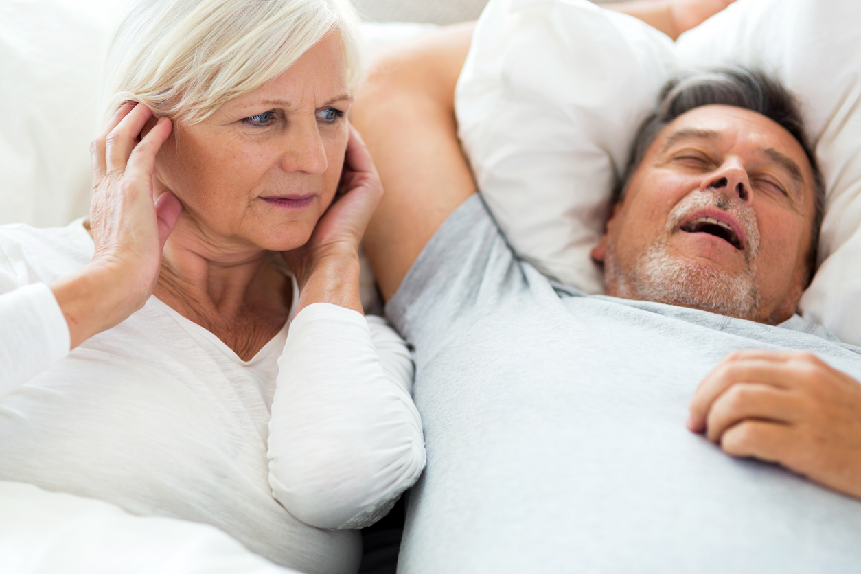 An elderly man snoring and a woman covering her ears.