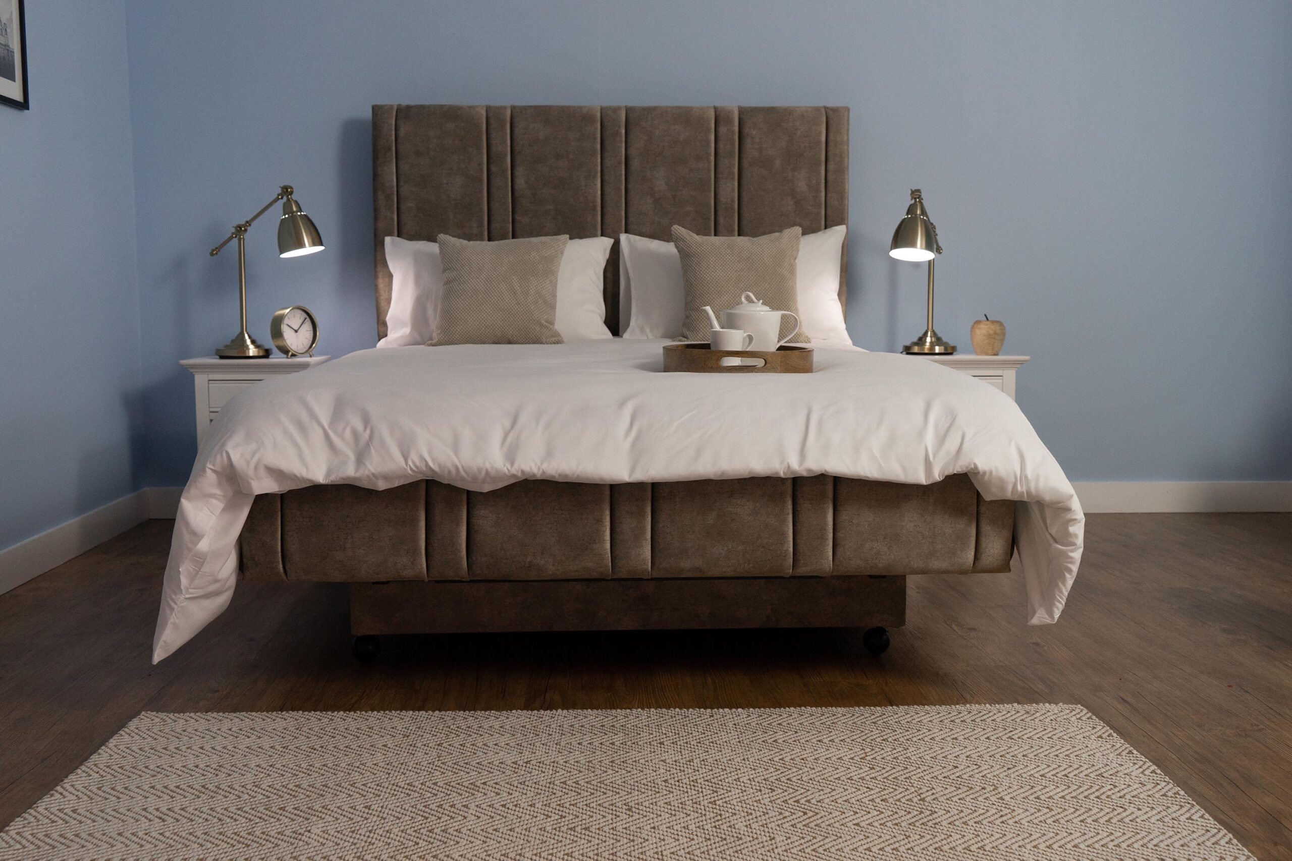 The Heritage Sandringham bed in a grey, beige fabric. The bed has white sheets and 2 beige cushions on it.