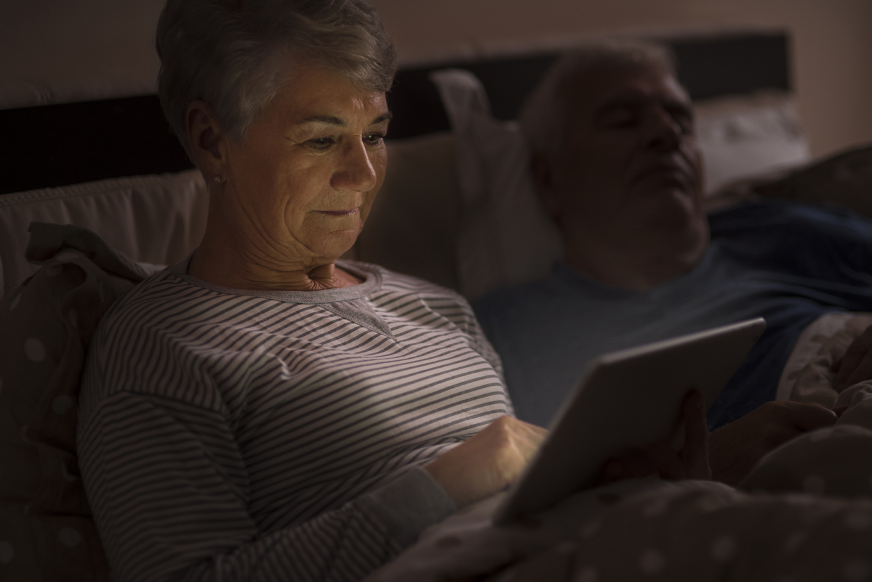 An elderly woman sat in bed looking at her tablet.