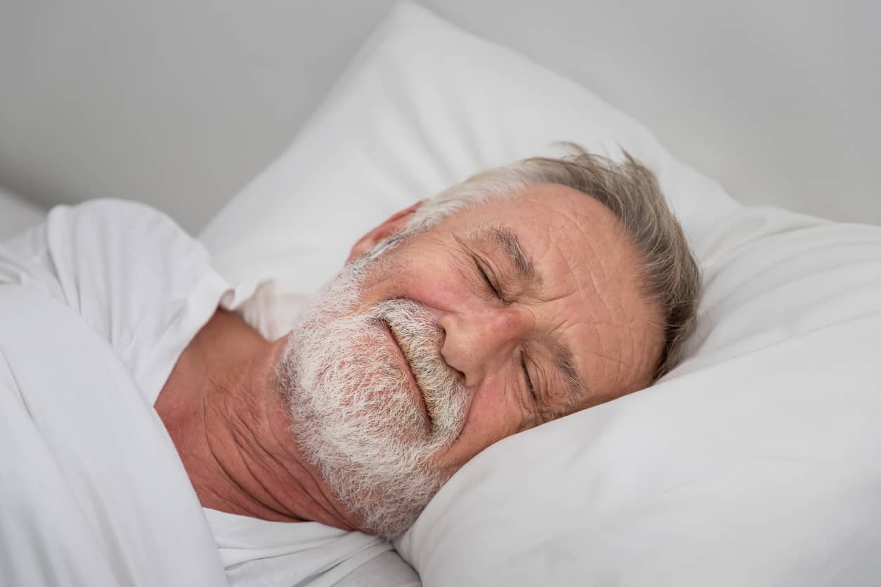 An elderly man sleeping peacefully in his electric adjustable bed.