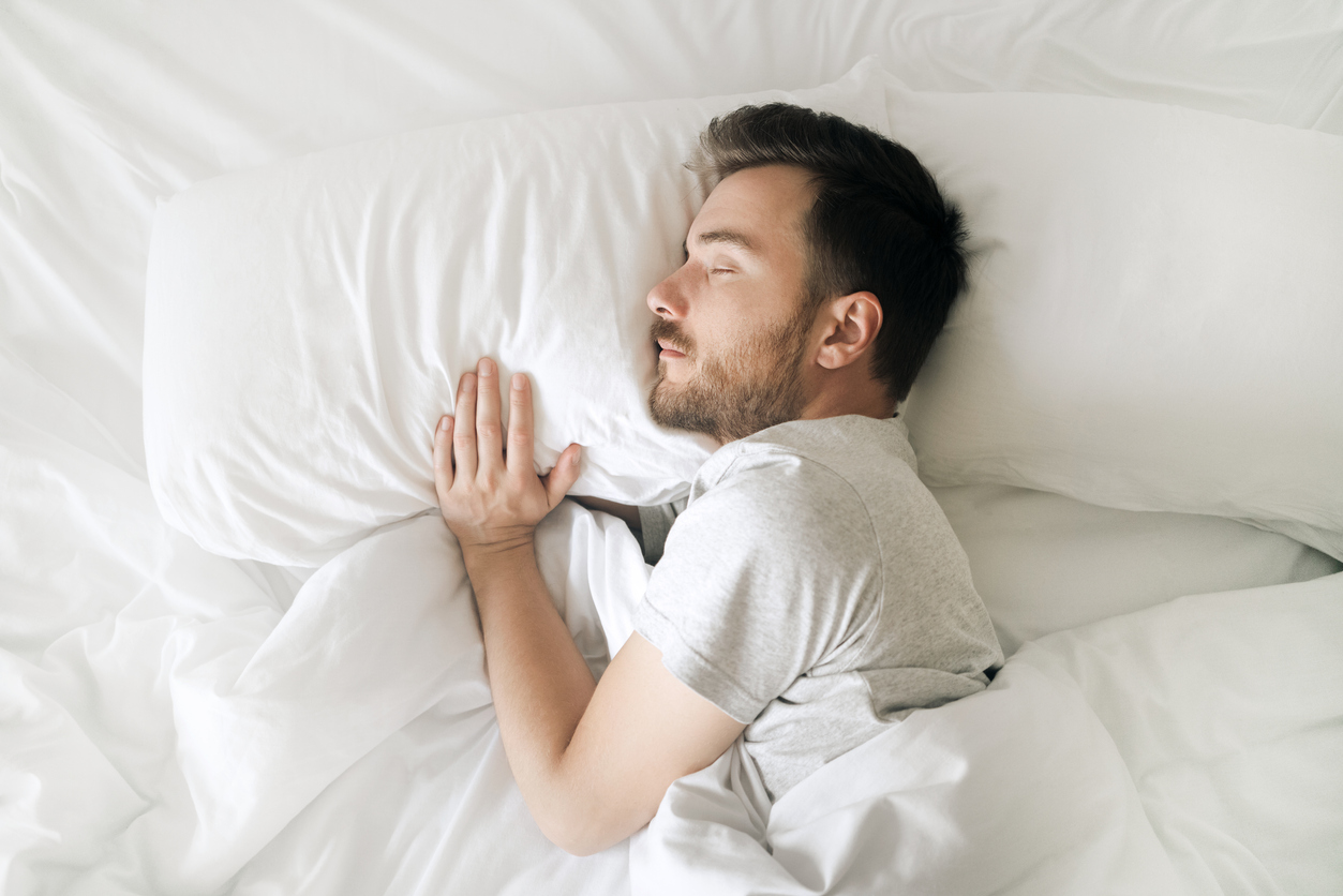 A top view of a sleeping man in white sheets of an adjustable bed.